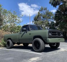 a green pick up truck parked in a parking lot next to some trees and bushes