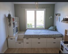 a small bedroom with a bed, bookcases and shelves on the wall next to an open window