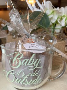 a baby it's cold outside mug with a bow on the handle and some flowers in the background