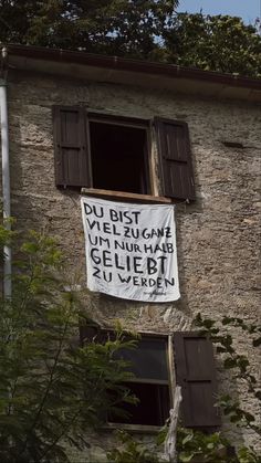 a sign hanging from the side of a building next to a window with shutters