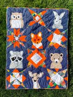 an orange and blue quilt with animals on it sitting in the middle of some grass