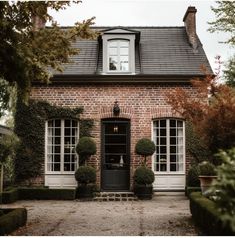 an old brick house with hedges and potted plants on the front door, surrounded by greenery