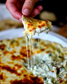 a hand holding a piece of pizza with cheese and spinach on it, over a white plate