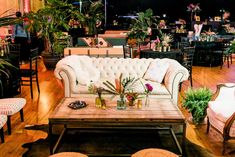 a living room filled with lots of furniture and plants on top of it's wooden floors