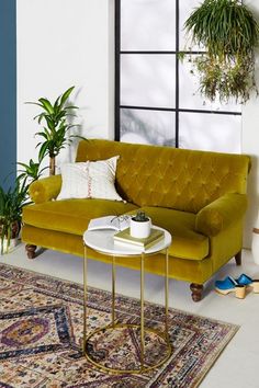 a yellow couch sitting on top of a rug next to a table and potted plants