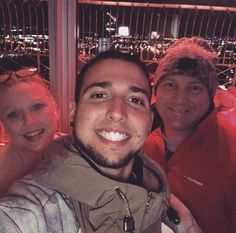 three people posing for a photo in front of a cityscape at night time