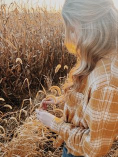 a girl standing in a field looking at her cell phone with corn stalks behind her