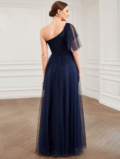 the back of a woman wearing a navy blue evening gown with one shoulder and sheer tulle