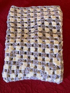 a crocheted blanket is laying on a red surface with white and brown squares