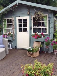 a wooden deck with chairs and potted plants next to a small shed filled with flowers