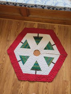 a red and white quilted table top with trees on the center, sitting on a wooden floor