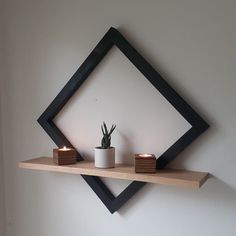 a shelf with two candles and a potted plant on it in front of a white wall