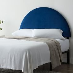 a bed with white sheets and blue headboard next to a plant in a vase