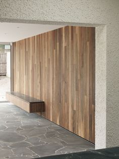 an empty bench in front of a wood paneled wall and concrete flooring on the side of a building