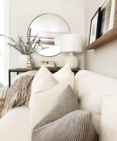 a living room with white couches and pillows on top of each other in front of a round mirror