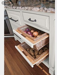 two baskets on the bottom shelf of a kitchen cabinet with potatoes and onions in it