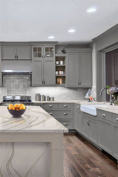 a large kitchen with gray cabinets and marble counter tops, along with a bowl of fruit on the island