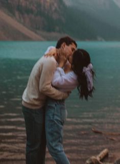 a man and woman kissing on the shore of a lake