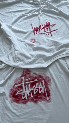 two white shirts with red spray paint on them