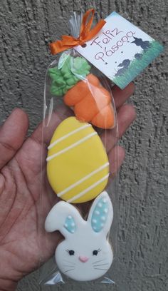 a hand holding a plastic easter egg, carrot and pineapple shaped cookie in it's package