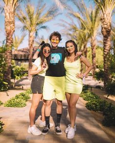 three young people posing for a photo in front of palm trees and bushes with their arms around each other