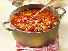 a large pot filled with stew on top of a table next to bread and spoons