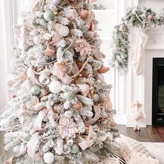 a white christmas tree with pink and green ornaments in the corner next to a fireplace