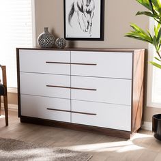 a white and brown dresser sitting in a living room next to a plant on top of a rug