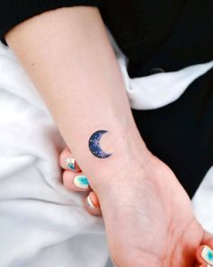 a woman's arm with a small crescent tattoo on her left wrist and the moon in the background