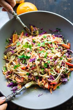 a person holding a fork in a bowl filled with coleslaw and carrots