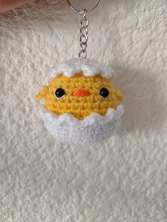 a crocheted chicken keychain hanging from a chain on a white surface