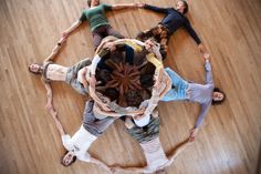 a group of people standing in a circle on top of a wooden floor with their hands together