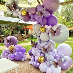 purple and white balloons are on display in the grass near a table with two butterfly figurines