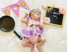 a baby wearing a tiara laying on top of a bed next to a frying pan