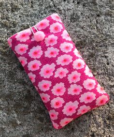 a pink and white flowered pouch sitting on top of a cement ground next to a cell phone