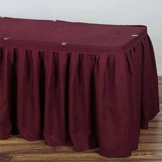 a table with a red cover on it in front of a white wall and wooden floor