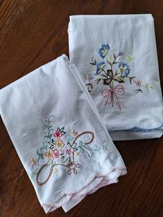 two embroidered napkins sitting on top of a wooden table