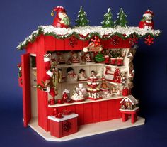 a red and white christmas display case with santa clause decorations on the top, snowflakes hanging from it's roof