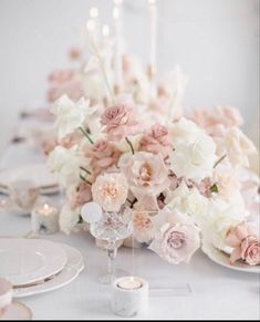 the table is set with white and pink flowers, candles, and plates on it