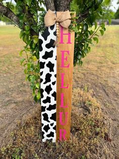 a wooden sign that says hello kitty on it next to a tree with a bow