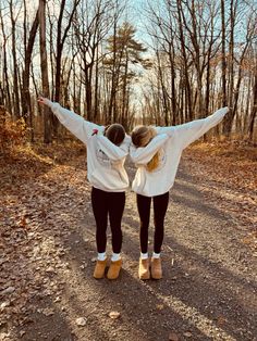 two girls are standing on the road with their arms in the air