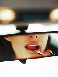 a woman is brushing her teeth in the rear view mirror while holding a cell phone