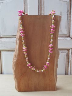 pink and green flowers are on a wooden stand next to a white door with an unfinished piece of wood in the background