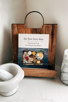 the first forty days cookbook sits on a wooden stand next to two bowls and a salt shaker