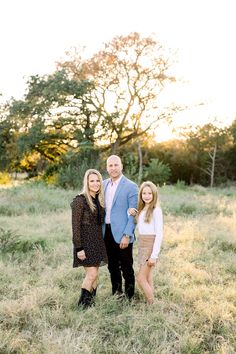 an older man and two younger women posing for a photo in a field with trees