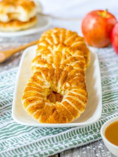 an apple pie on a white plate next to some apples and dipping sauce in small bowls