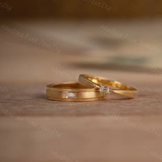 two gold wedding rings sitting on top of a wooden table