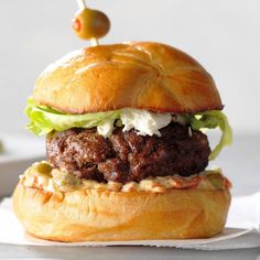 a hamburger sitting on top of a bun covered in lettuce and cheese with a toothpick sticking out of it