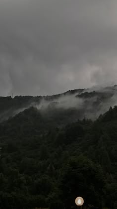 the mountains are covered in fog and low lying clouds on a gloomy day,