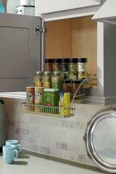 an open cabinet in a kitchen with spices and coffee mugs on the counter top